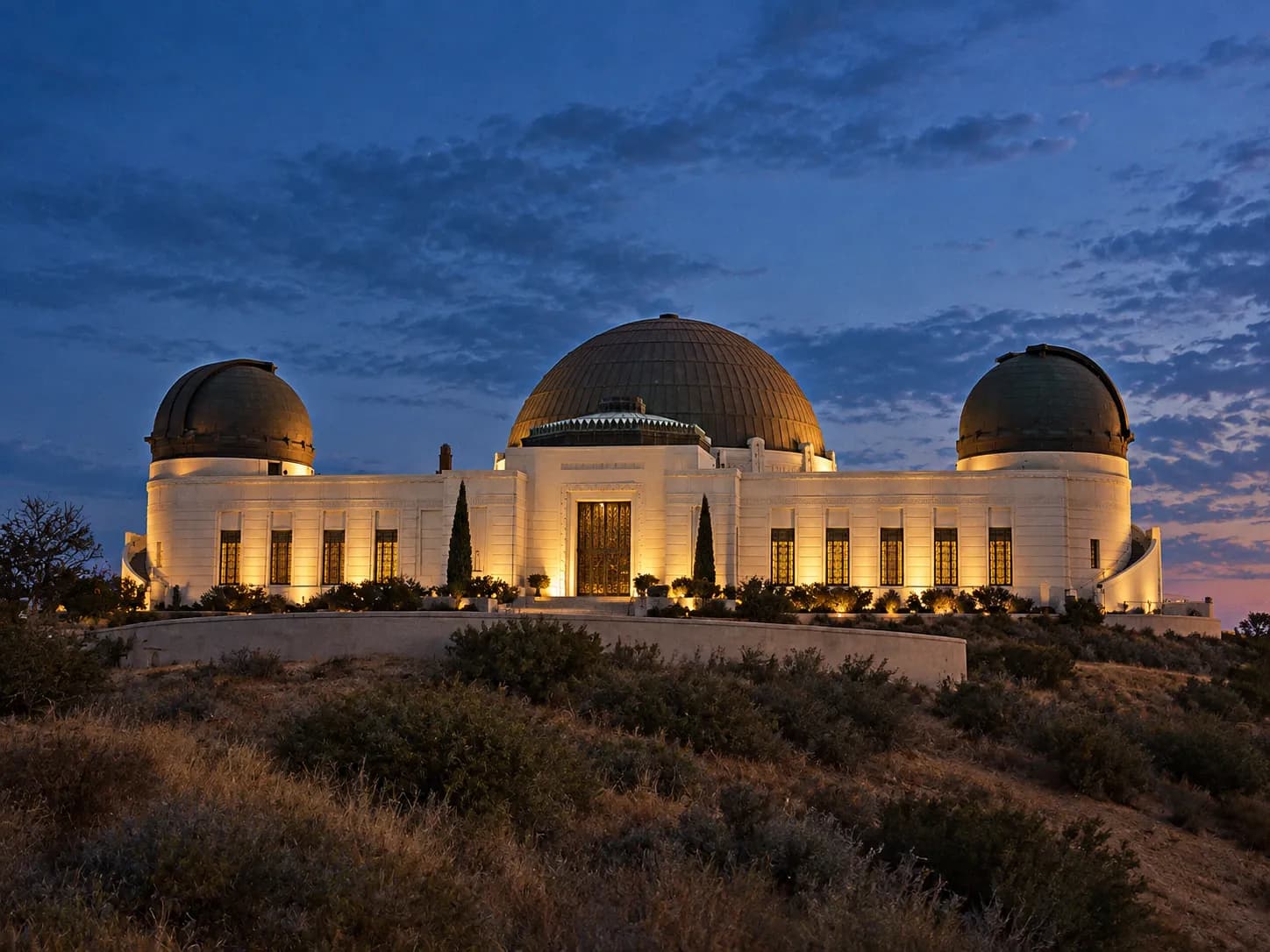 A domed art deco observatory building on a hillside under a darkening sky