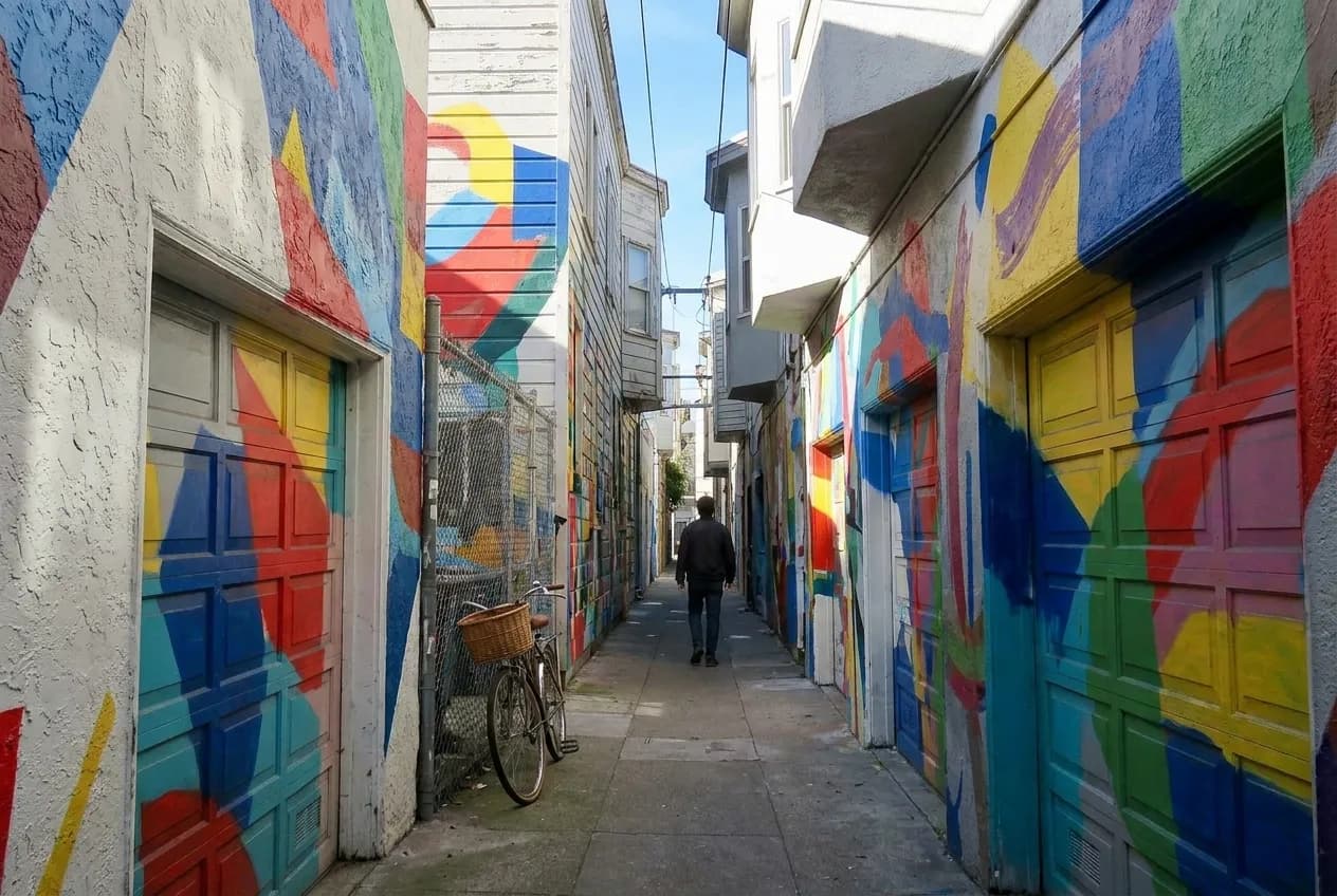 A narrow alley with painted murals covering both walls and a garage door