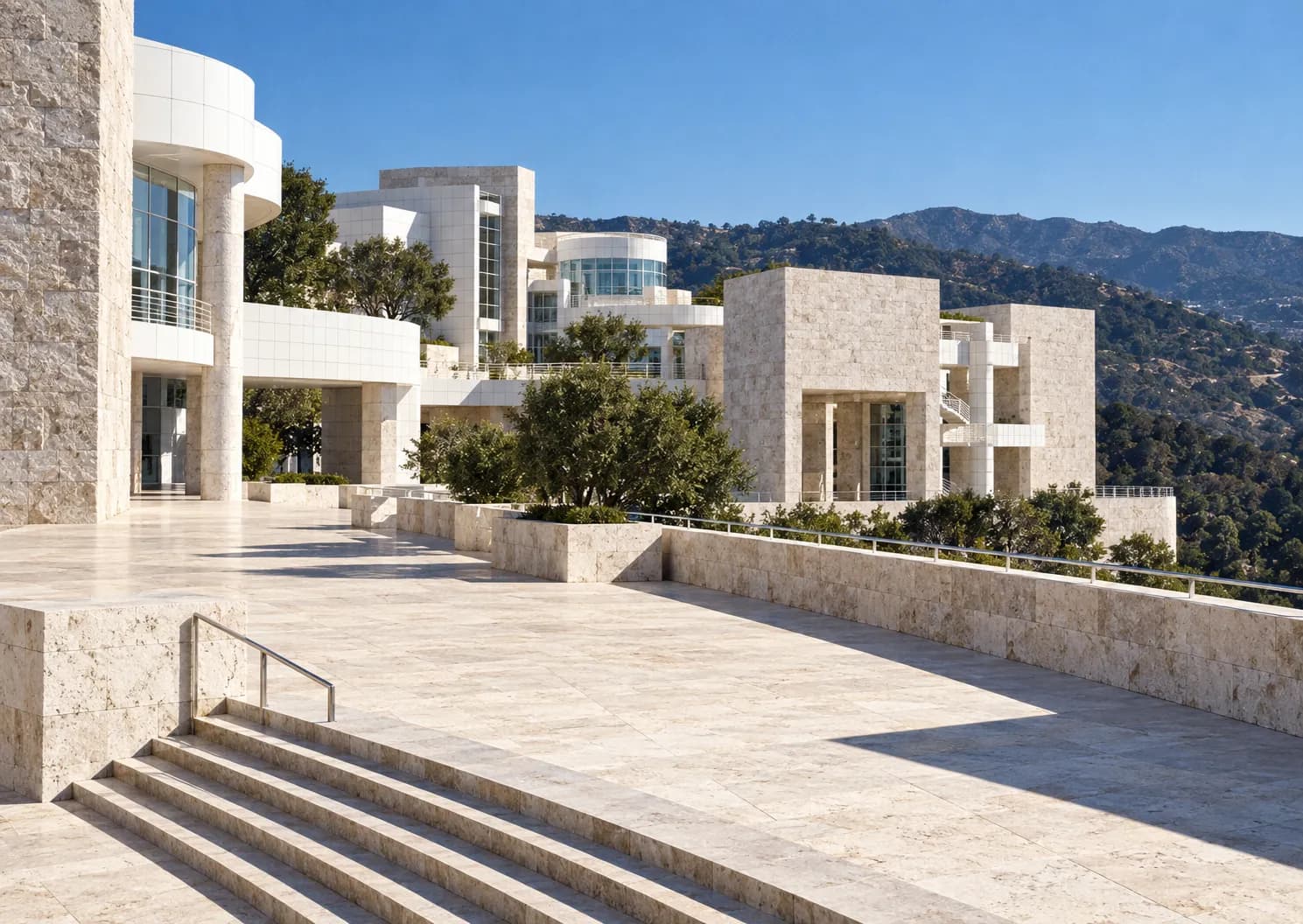 Pale stone pavilions and terraces of a hilltop museum against a bright sky
