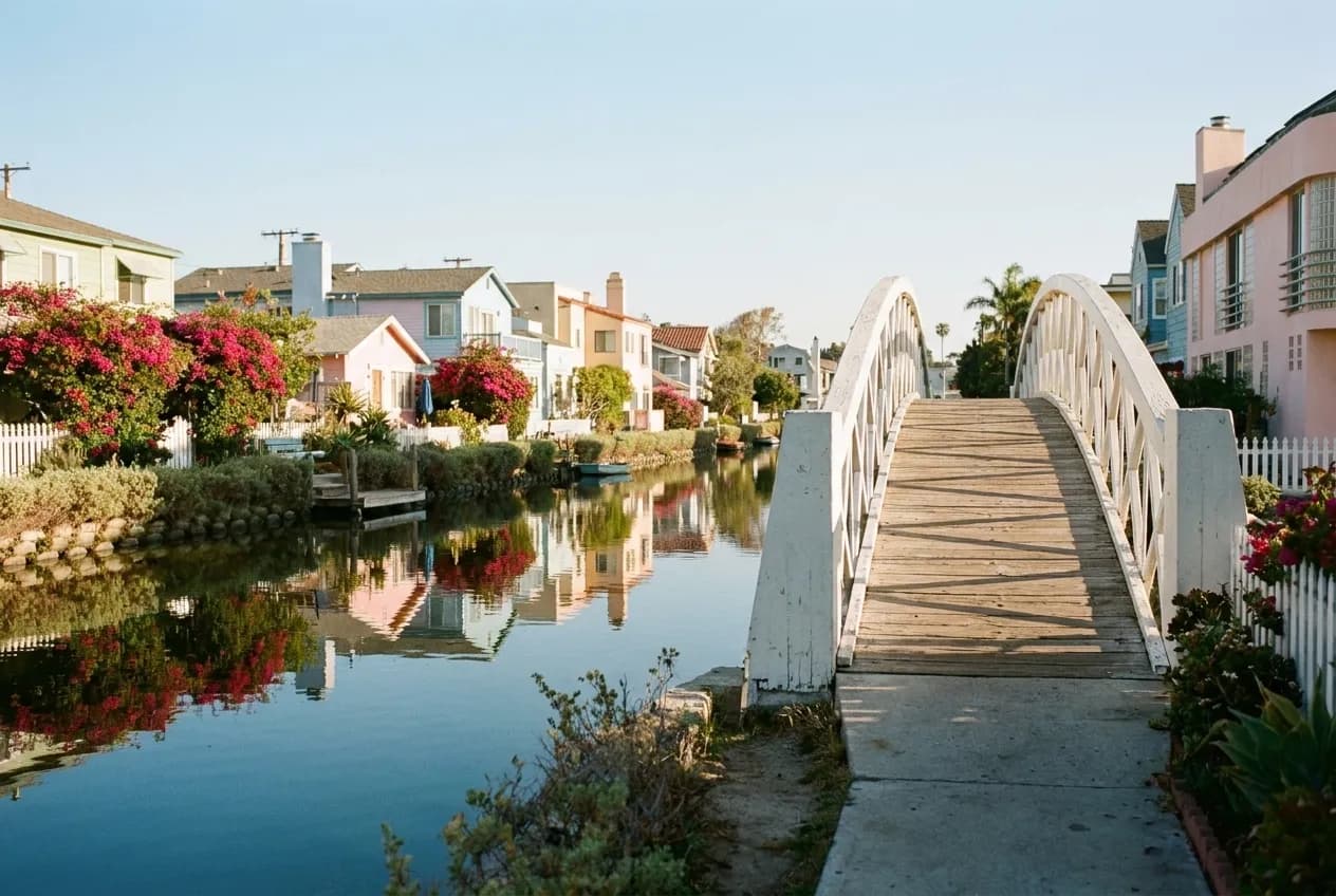 An arched wooden footbridge crossing a calm canal lined with colorful bungalows in Venice, Los Angeles.