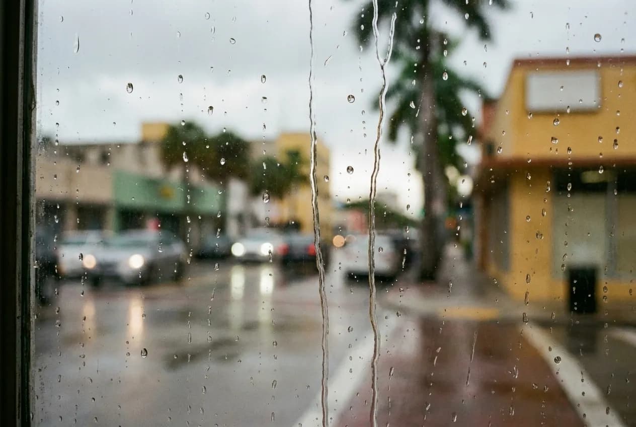 Rain beading and running down a pane of glass, the street beyond reduced to soft blocks of colour and light
