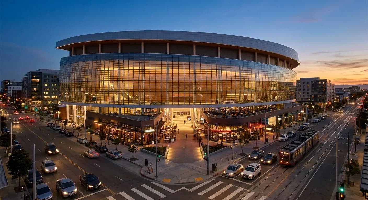 Chase Center's illuminated exterior at dusk with Thrive City plaza lights glowing and Third Street Muni tracks in foreground