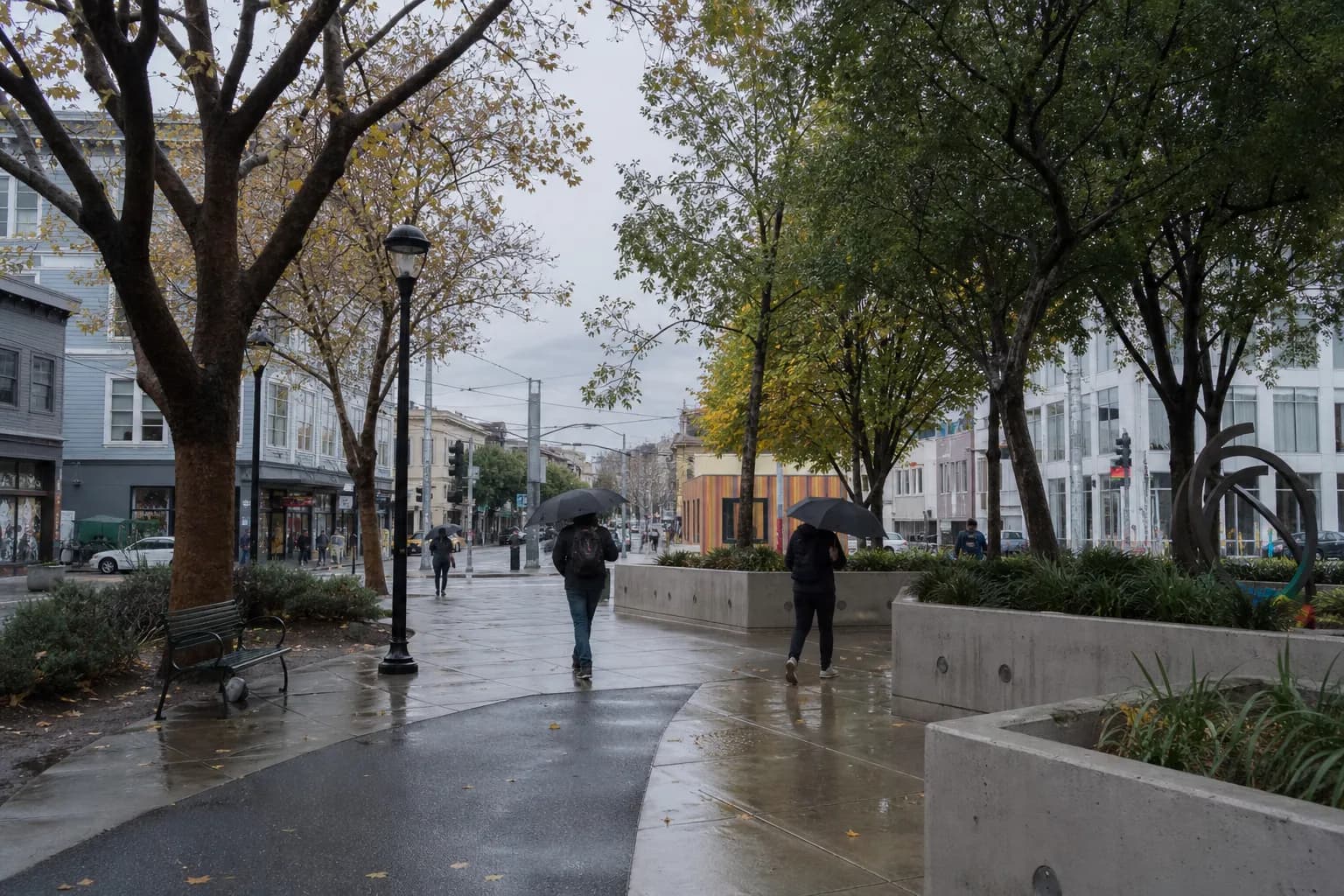 Wide view of a wet pedestrian plaza near Hayes Valley with trees and people walking under umbrellas
