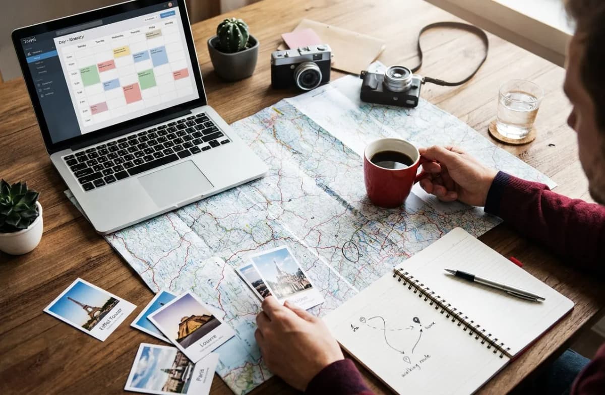 A traveler arranges a visual day-by-day itinerary on a laptop over a paper map and coffee.