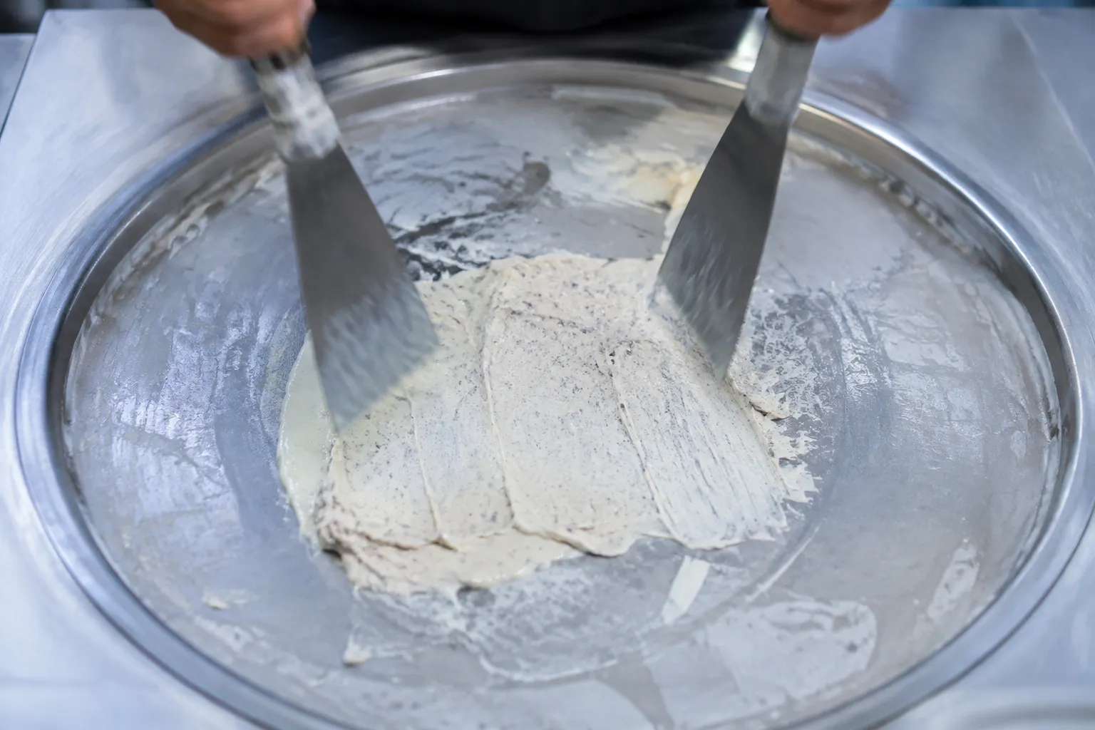 Overhead view of cream mixture being scraped on a frozen steel plate for rolled ice cream