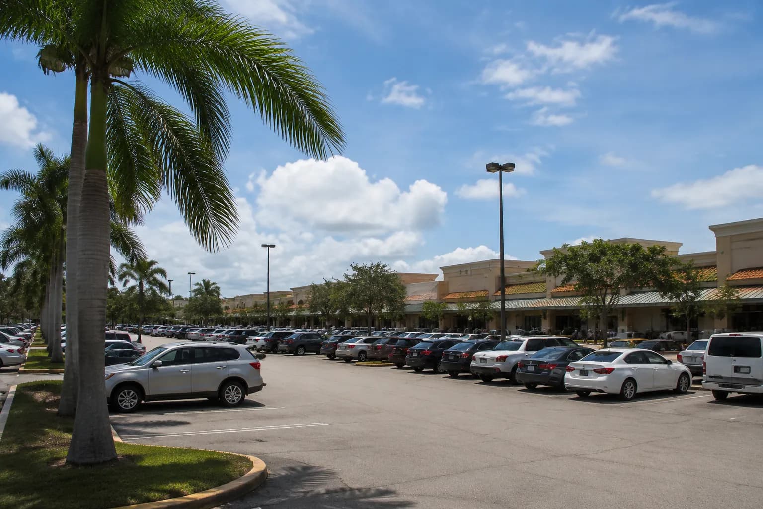 Strip mall parking lot in Kendall with parked cars and shoppers under afternoon sun