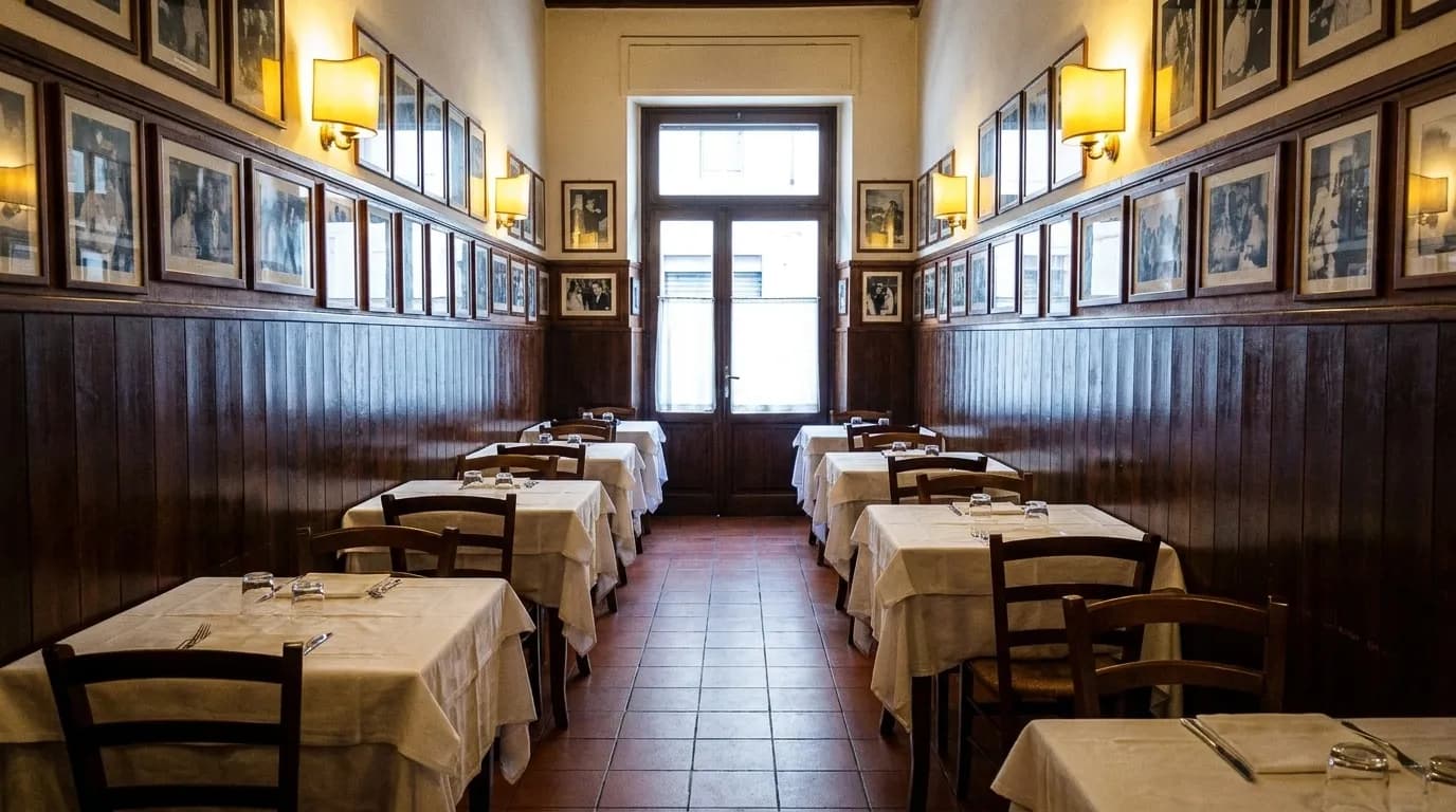 A narrow old-school restaurant dining room with white tablecloths, wood panelling and framed photographs on the wall, chairs tucked in before service