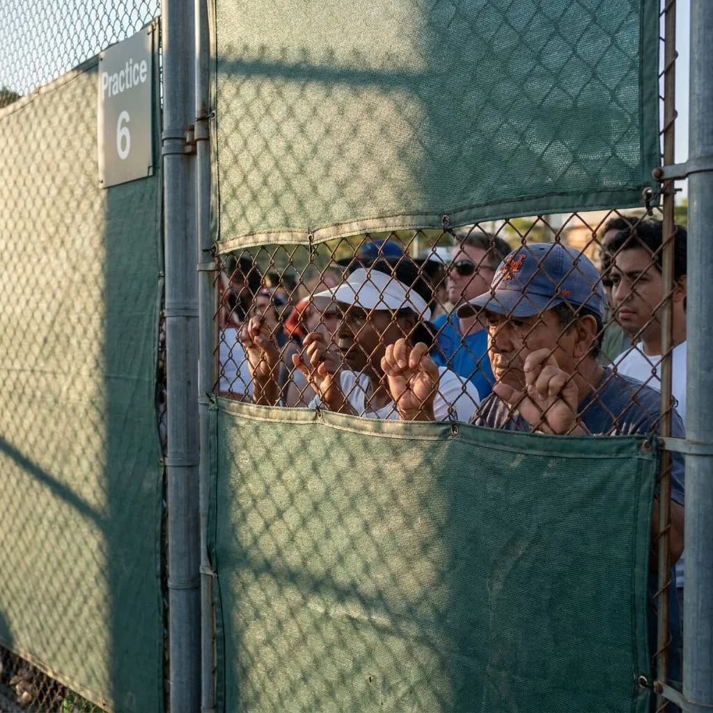 US Open 2026 First Weekend: The Flushing Meadows Circuit Beyond Center Court — Close view of hands gripping the chain-link fence at Practice Court 6, late afte