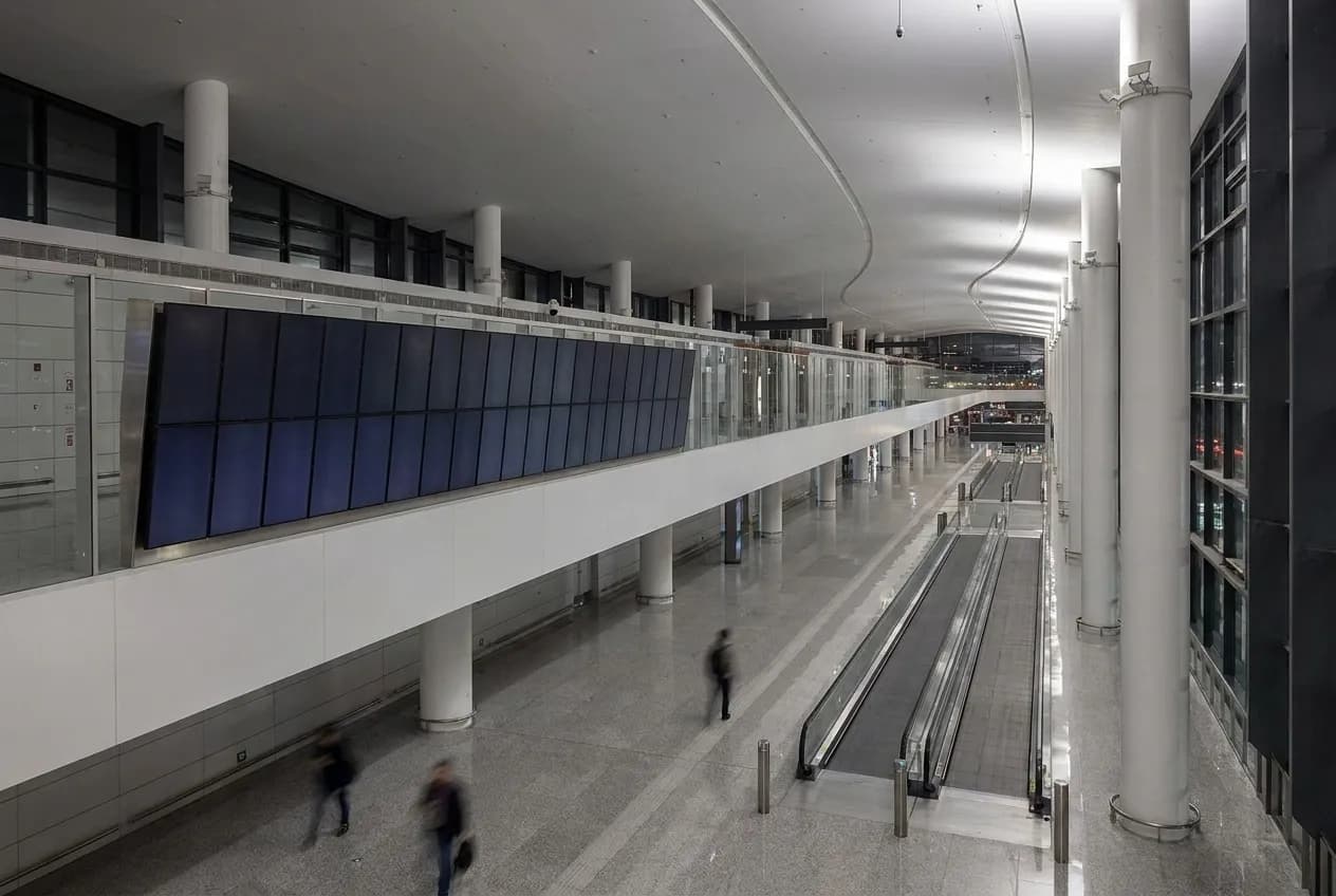 An airport departure board wall with blank panels above a terminal walkway