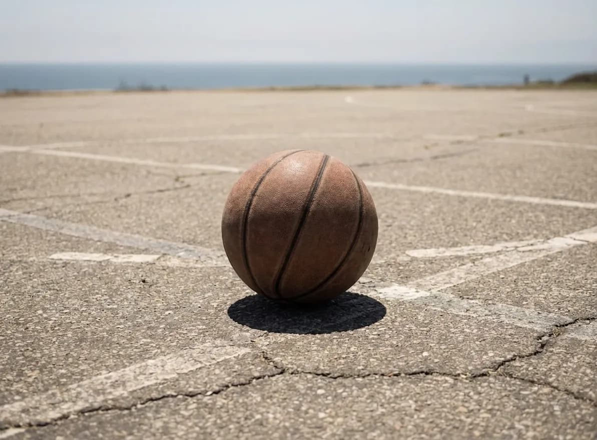 Worn outdoor basketball on asphalt court with faint painted lines and distant ocean view