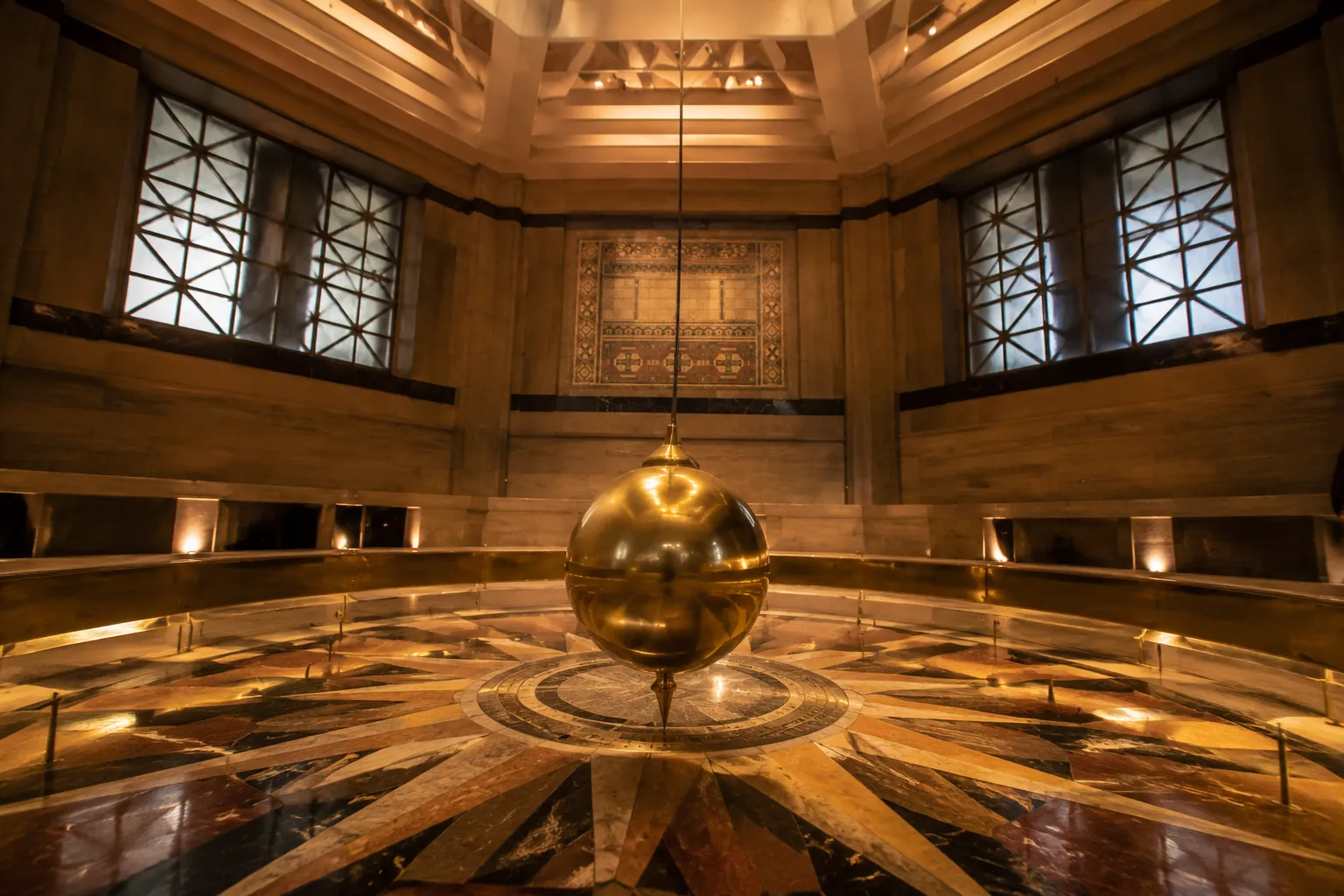 Brass Foucault pendulum hanging in the Griffith Observatory rotunda with geometric floor pattern below