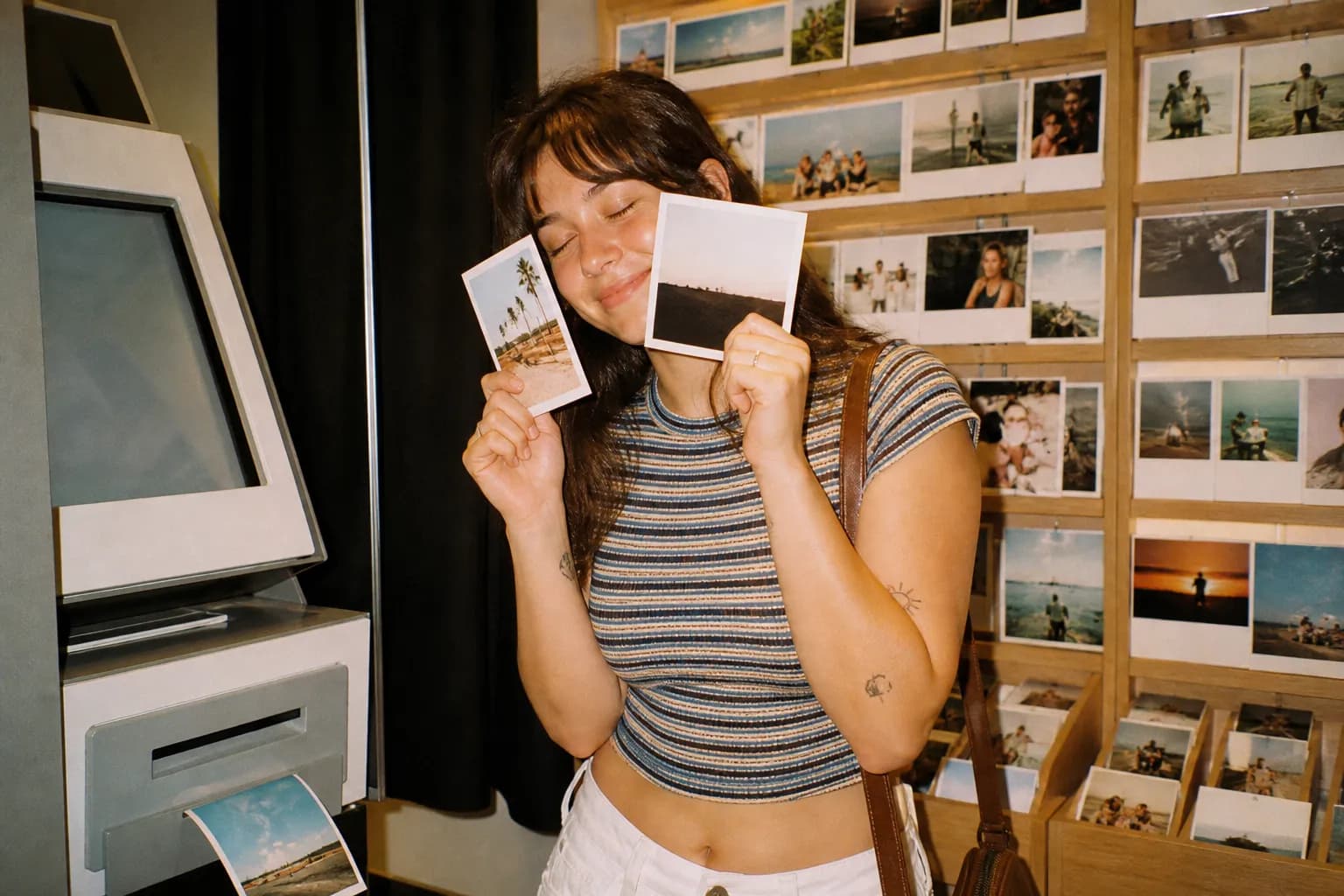 A stack of freshly printed photos beside a self-service photo kiosk in a store