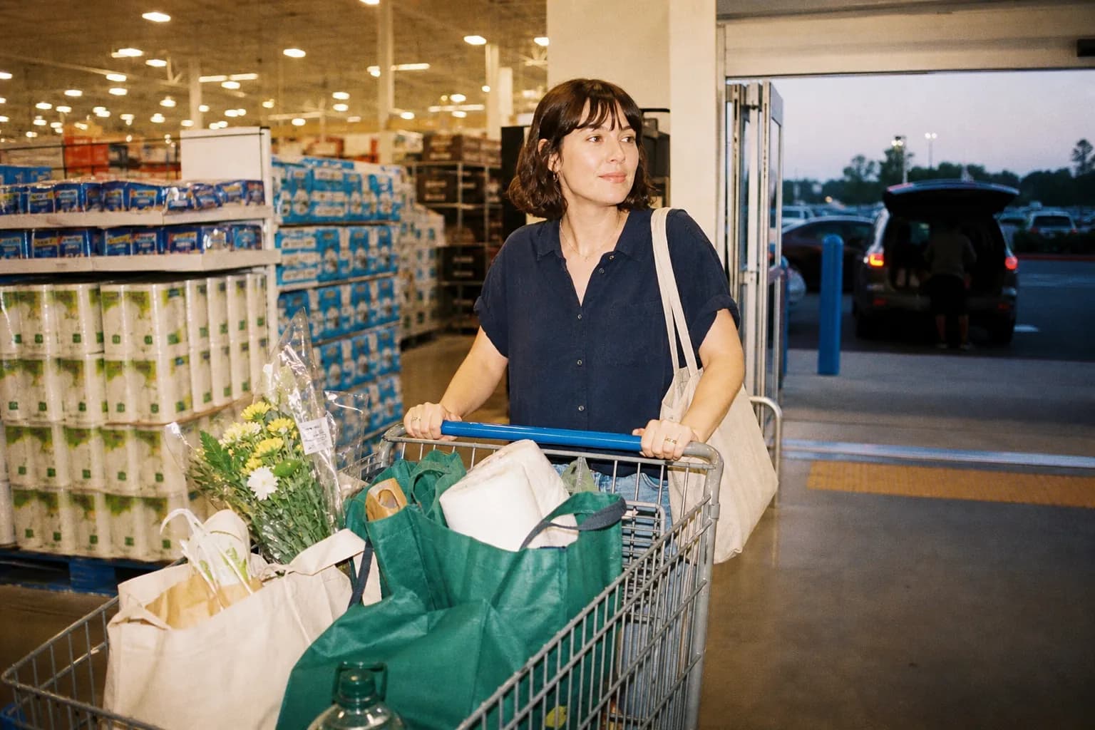 A shopper pushing a full cart of groceries and household goods through a wide, brightly lit big-box store aisle