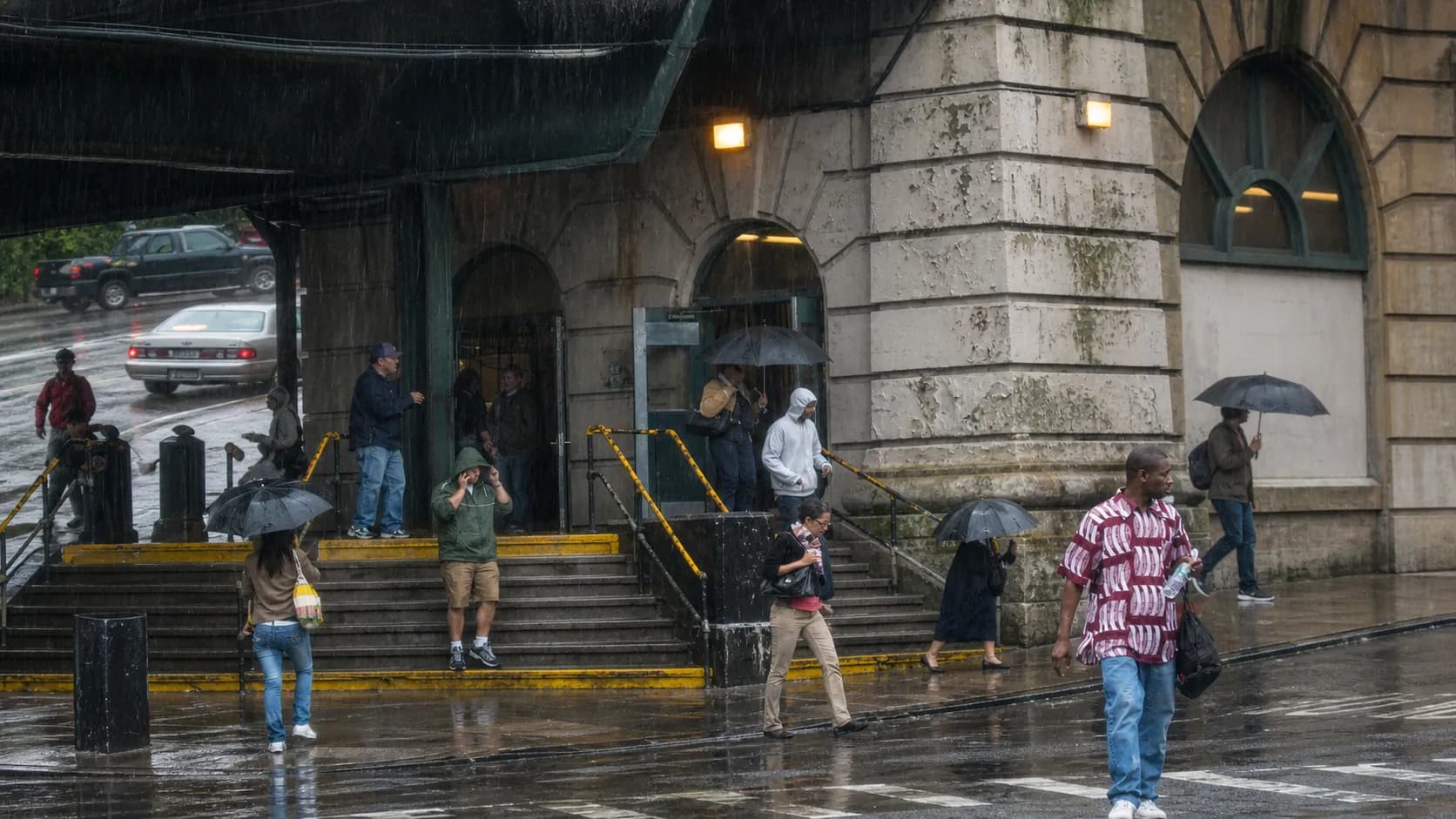 Commuters shelter near a New York City subway entrance during heavy rain.