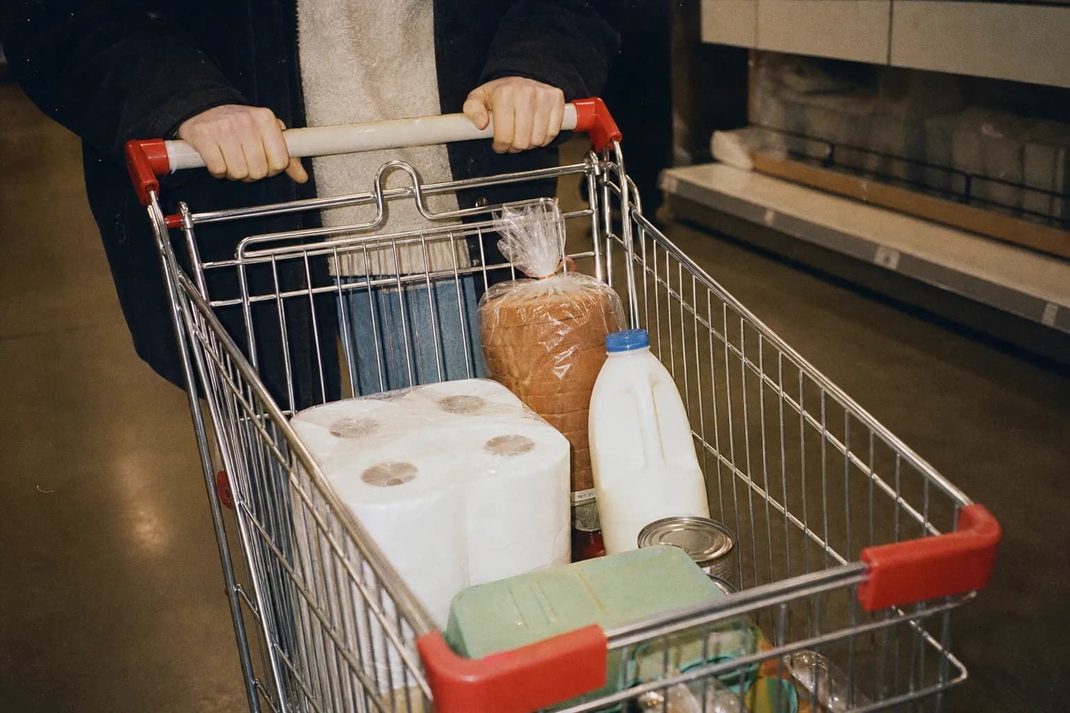 A shopping cart holding a few budget items in a bright discount store aisle