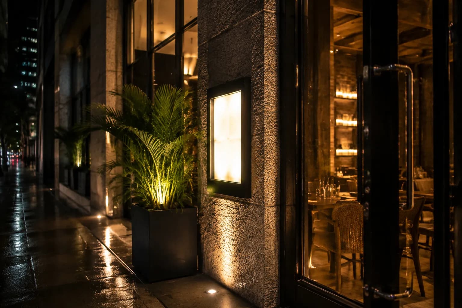 Modern restaurant entrance in Brickell at night with illuminated interior and wet pavement reflections