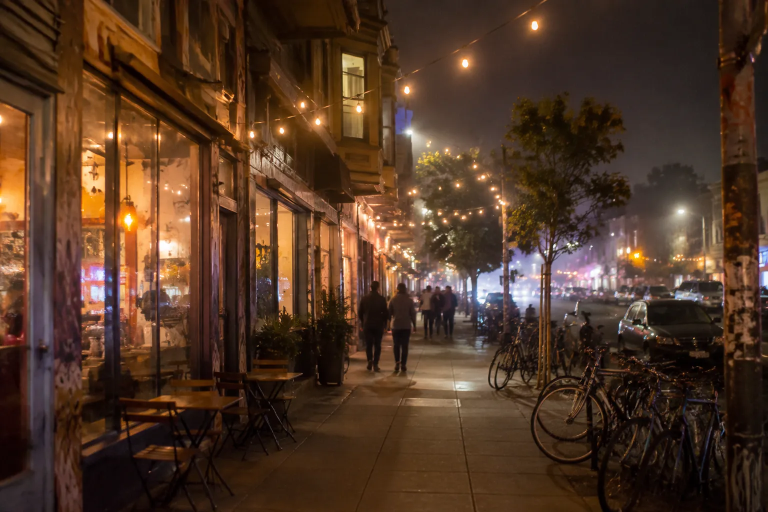 Valencia Street at night in San Francisco with lit cafes, outdoor seating, and fog softening streetlights