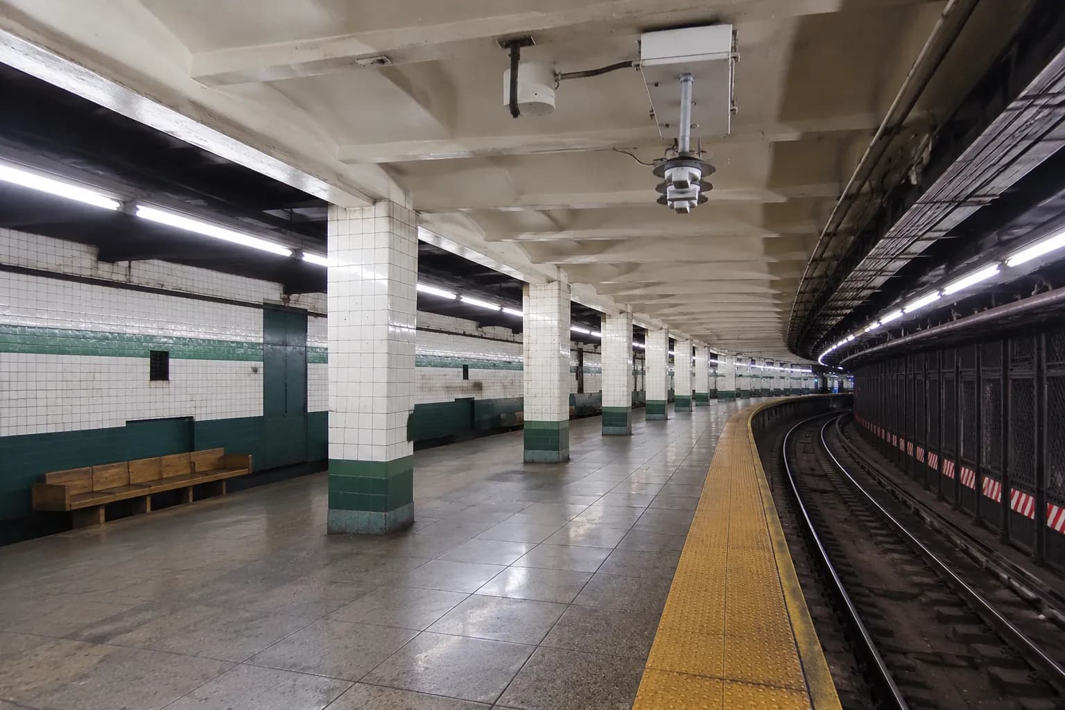 An empty G train subway platform in Brooklyn with tiled walls and light filtering from above.