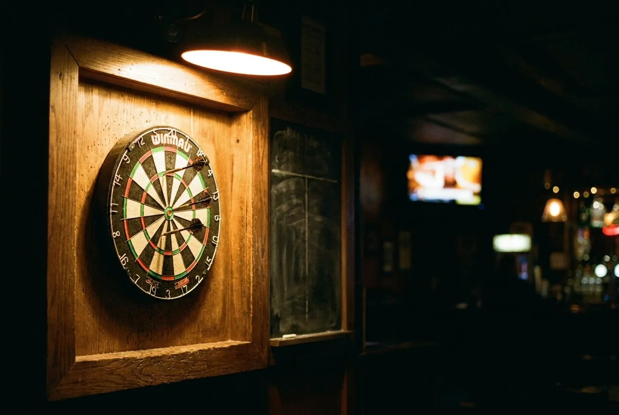A lit dartboard lane in a dark bar with a scoreboard chalked beside it