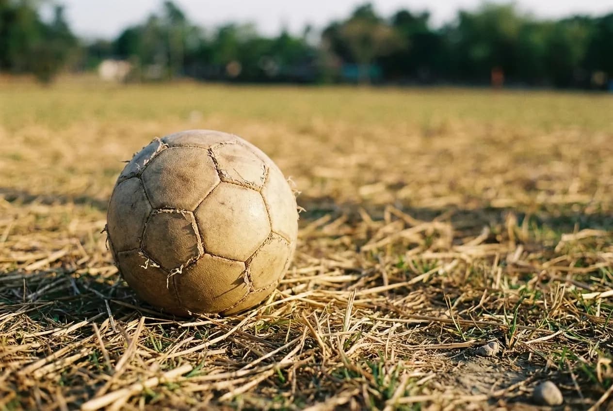 A worn football resting on cut grass, the panels and stitching sharp in the foreground and the pitch falling out of focus behind