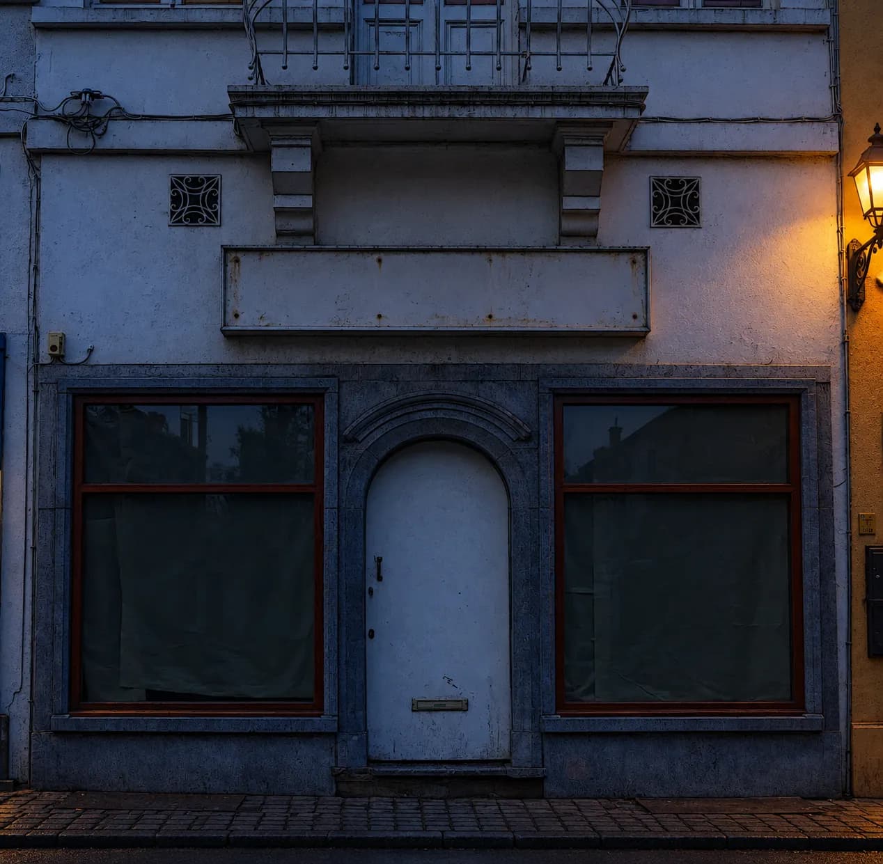 A closed storefront at dusk with dark windows and an empty pavement