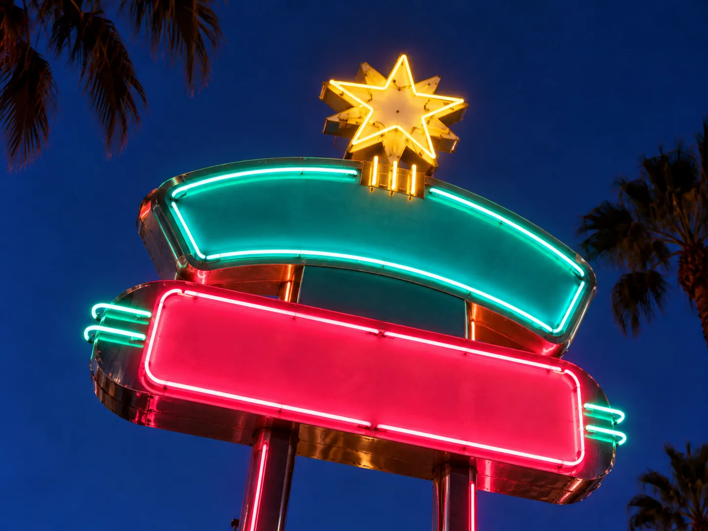 A neon-lit mid-century motel sign against a darkening sky