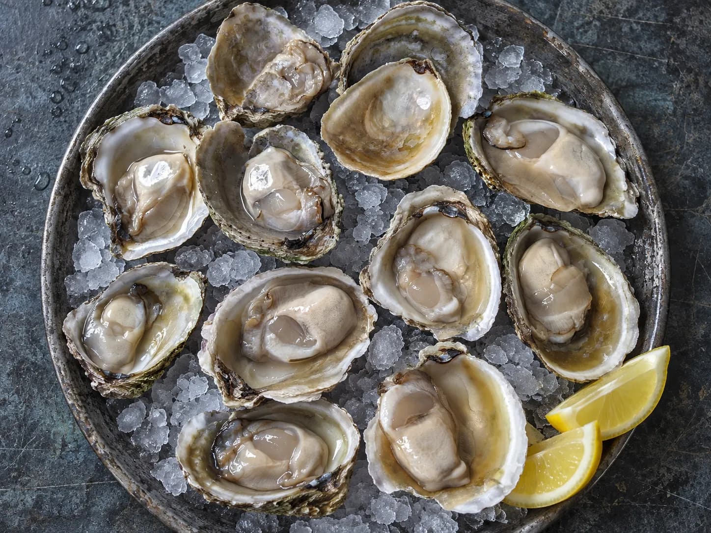 Oysters on crushed ice arranged on a metal tray with lemon wedges