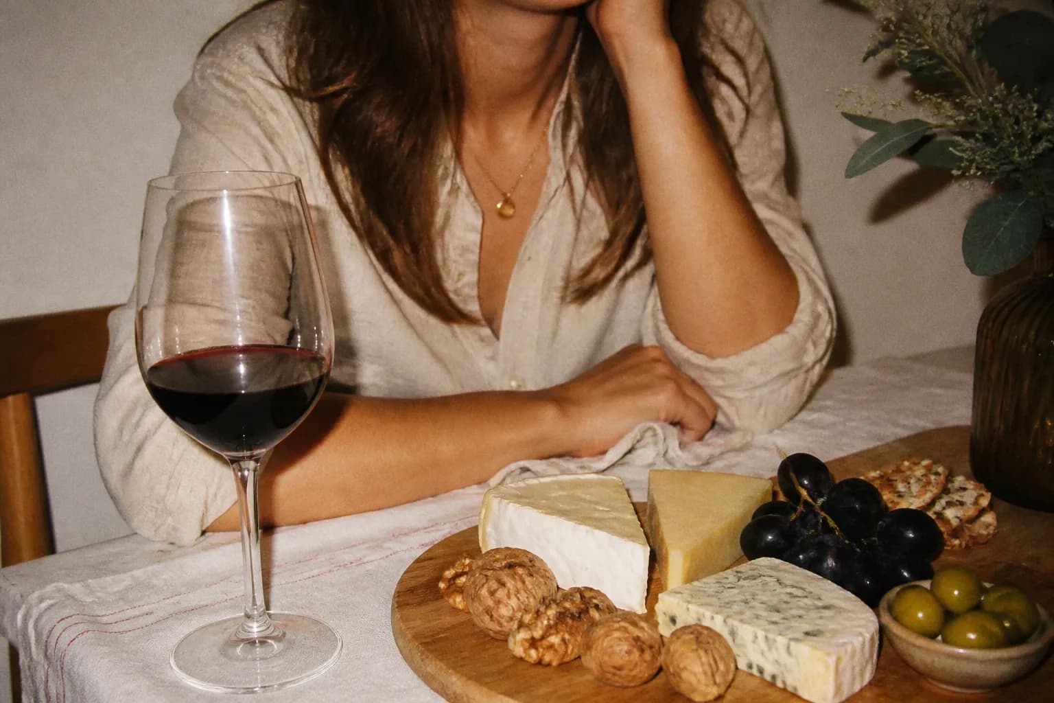 A glass of wine beside a wooden board with assorted cheeses and grapes