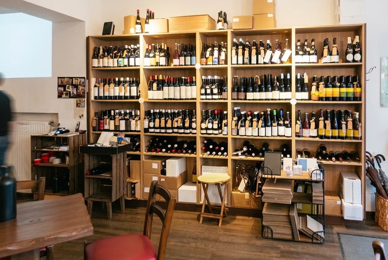 A narrow wine shop interior with bottles shelved floor to ceiling and a small standing counter