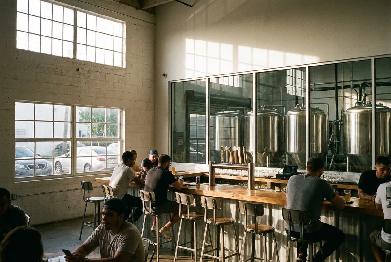 Fermentation tanks visible behind glass in a Wynwood brewery taproom with bar seating and industrial windows