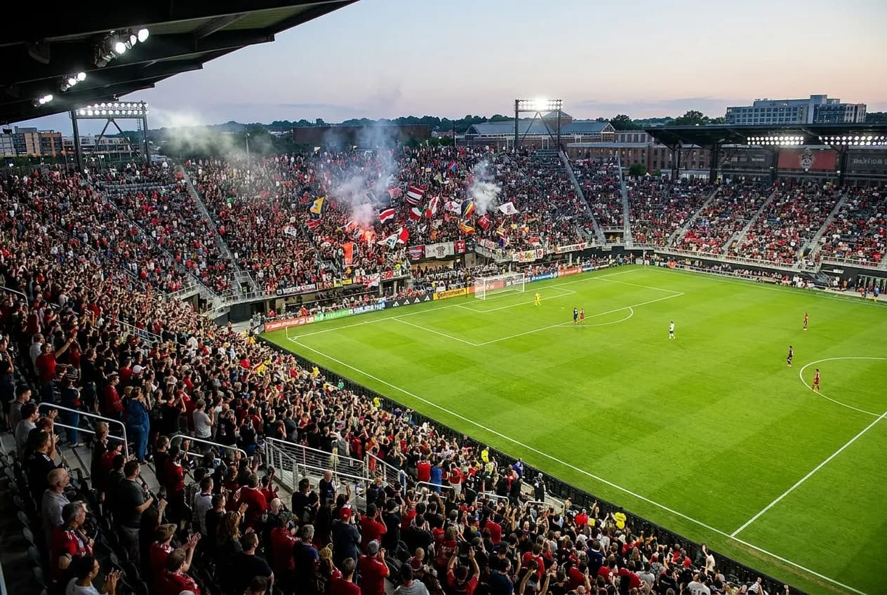 A modern soccer-specific stadium bowl with a green pitch, steep stands close to the field, floodlights and a full evening crowd