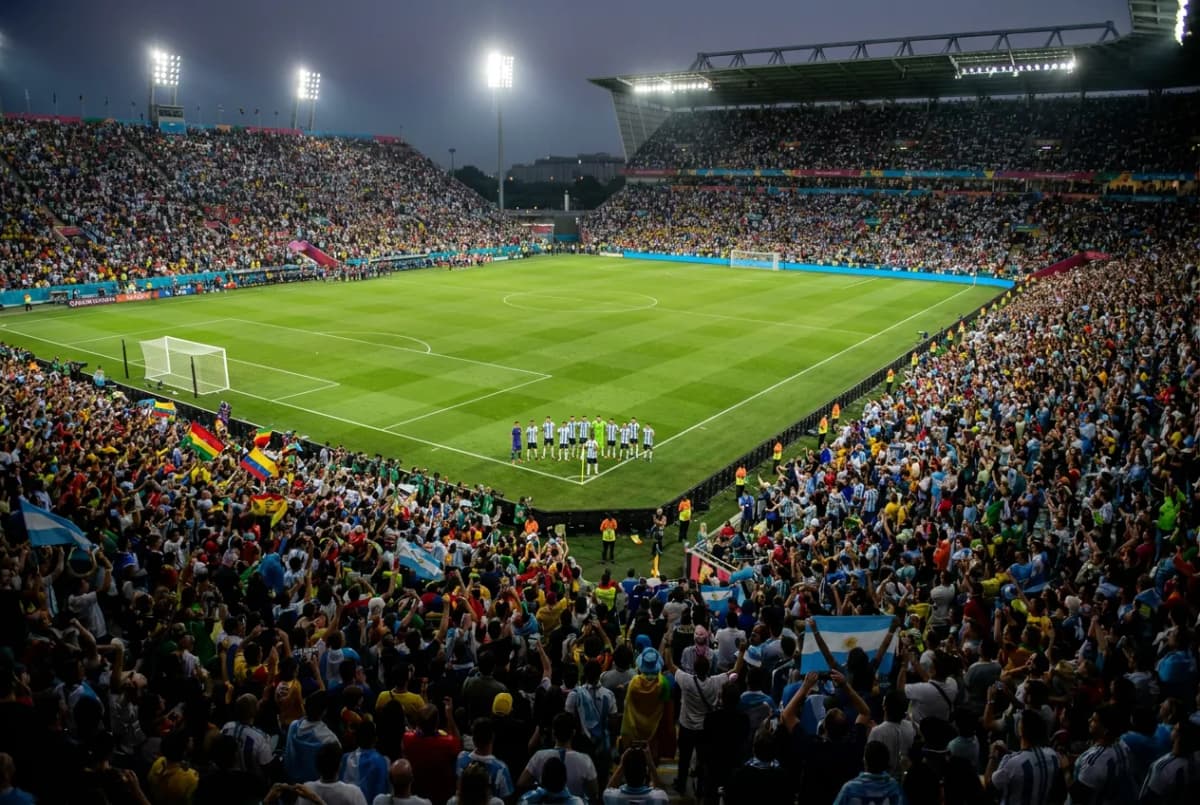 A packed floodlit stadium at night during a World Cup match with two teams lined up on the pitch