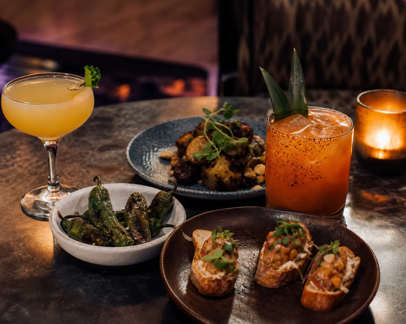 Two cocktails and several shared tapas plates on a small table