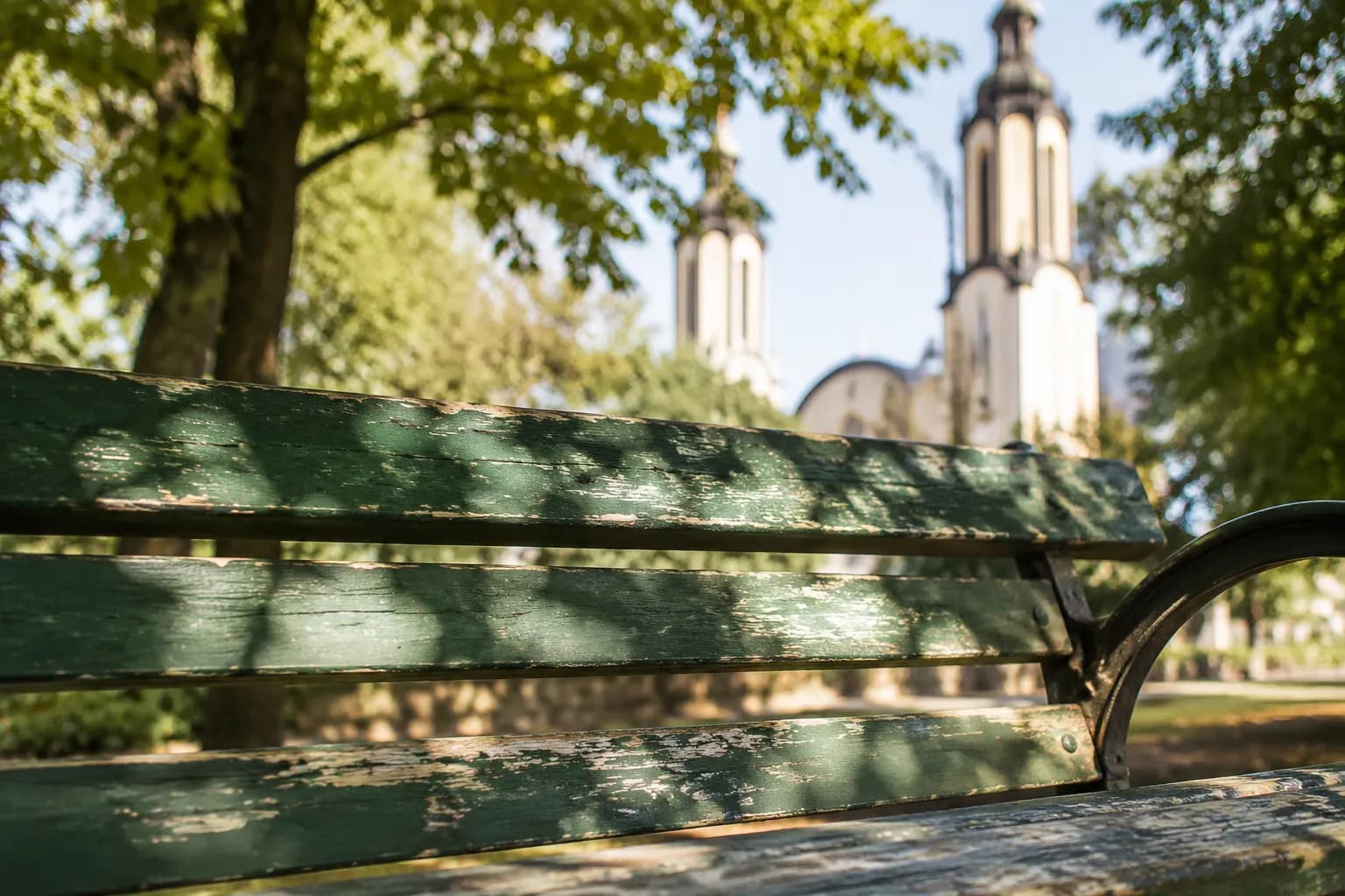 Park bench in Washington Square Park with dappled morning light and church towers beyond